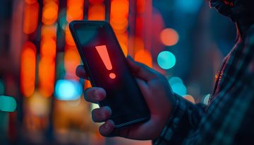 Hand holding smartphone displaying red exclamation mark against