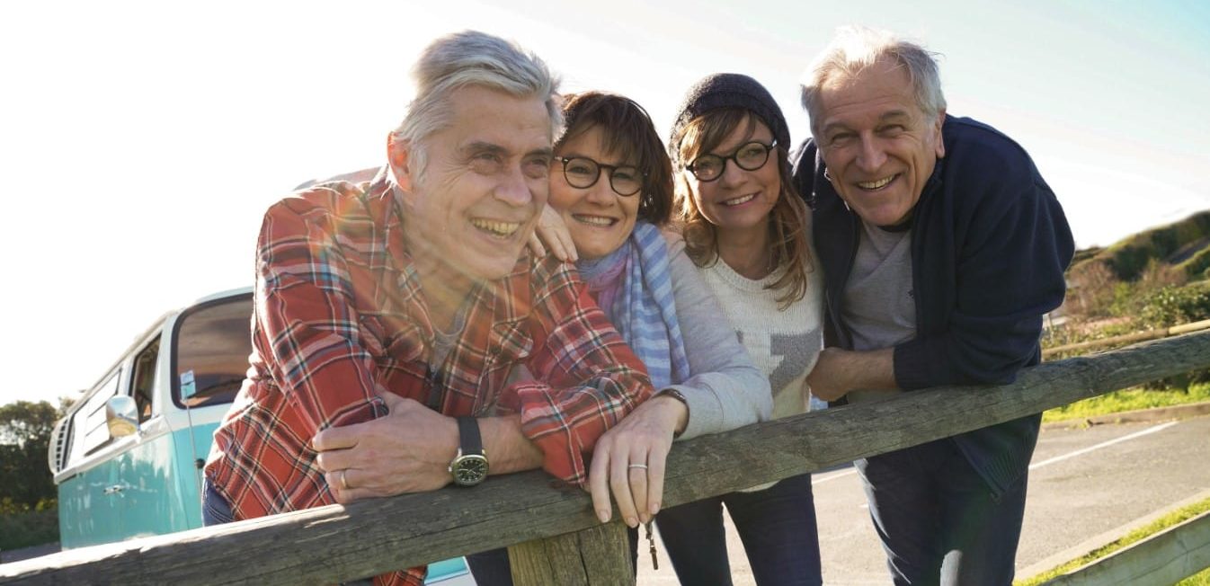 Senior friends on a road trip leaning on fence by the sea