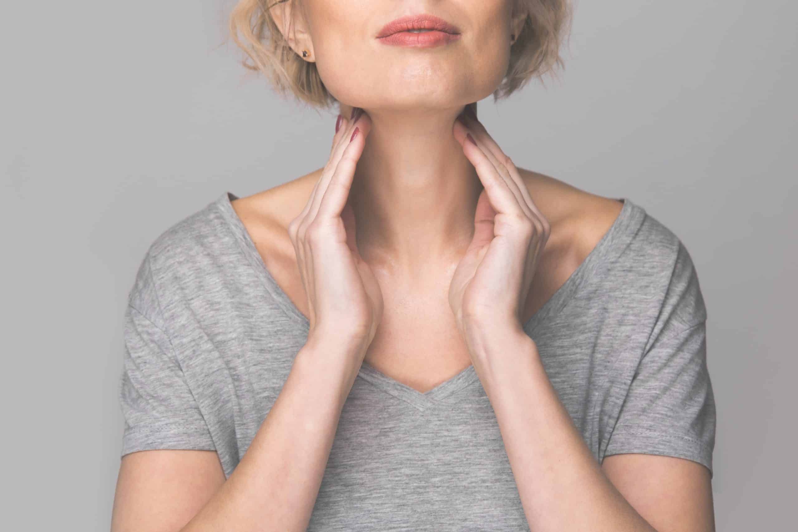 Female checking thyroid gland by herself. Close up of woman in white t- shirt touching neck with red spot. Thyroid disorder includes goiter, hyperthyroid, hypothyroid, tumor or cancer. Health care.