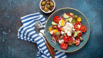 Greek fresh healthy colorful salad with feta cheese, vegetables, olives in blue ceramic bowl on rustic concrete background top view, Mediterranean diet, traditional cuisine of Greece