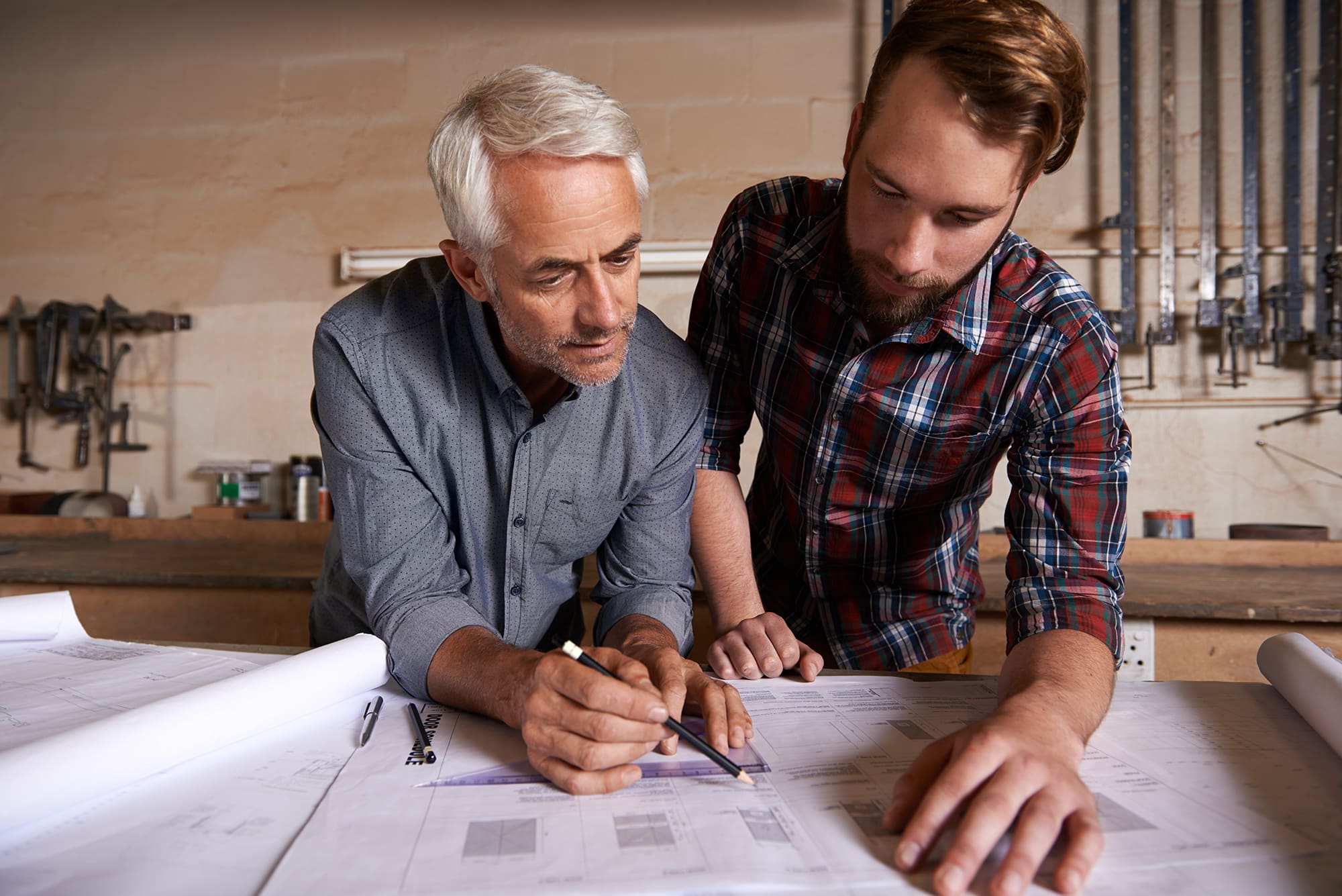 Architect team, working on blueprint in workshop and designer for engineering collaboration. Senior in architecture with male trainee, work on remodeling project with floor plan paperwork and drawing