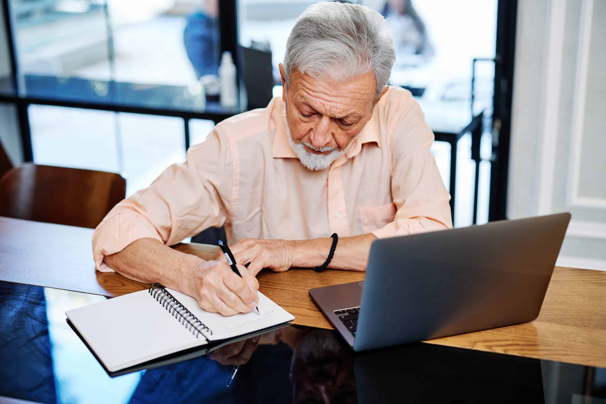 A happy senior student is sitting at home and writing down notes