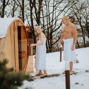 Senior woman in towel with her husband coming out from outdoor sauna during a cold winter day.